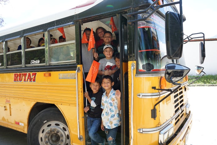 In Honduras, children smile as they depart from a school bus. 