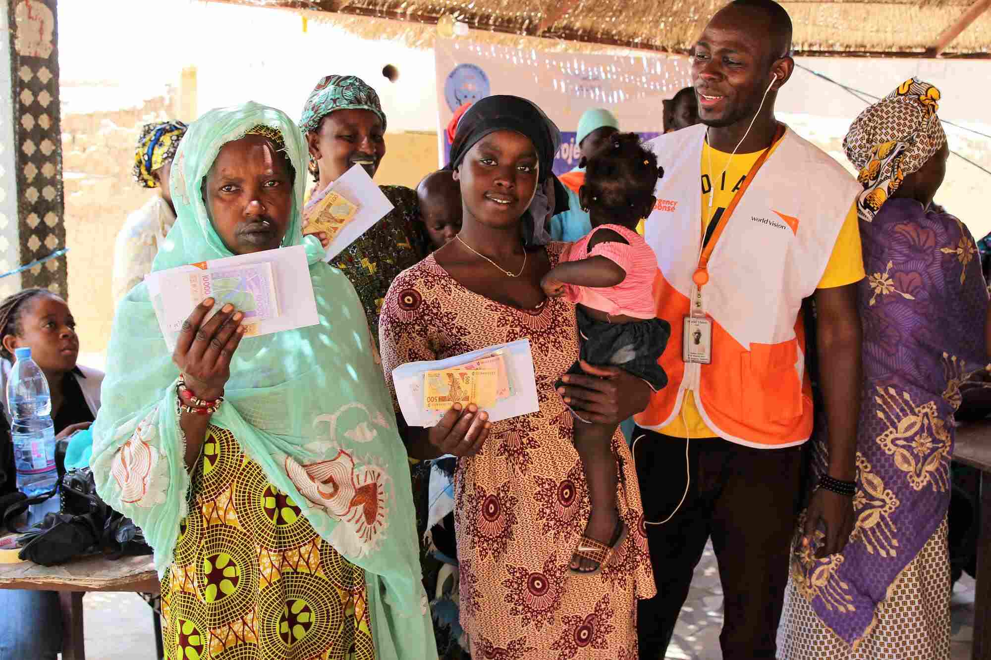 In Mali, two women stand beside a World Vision staff member and hold the cash they received through World Vision's cash distribution. One of the women holds her daughter. 