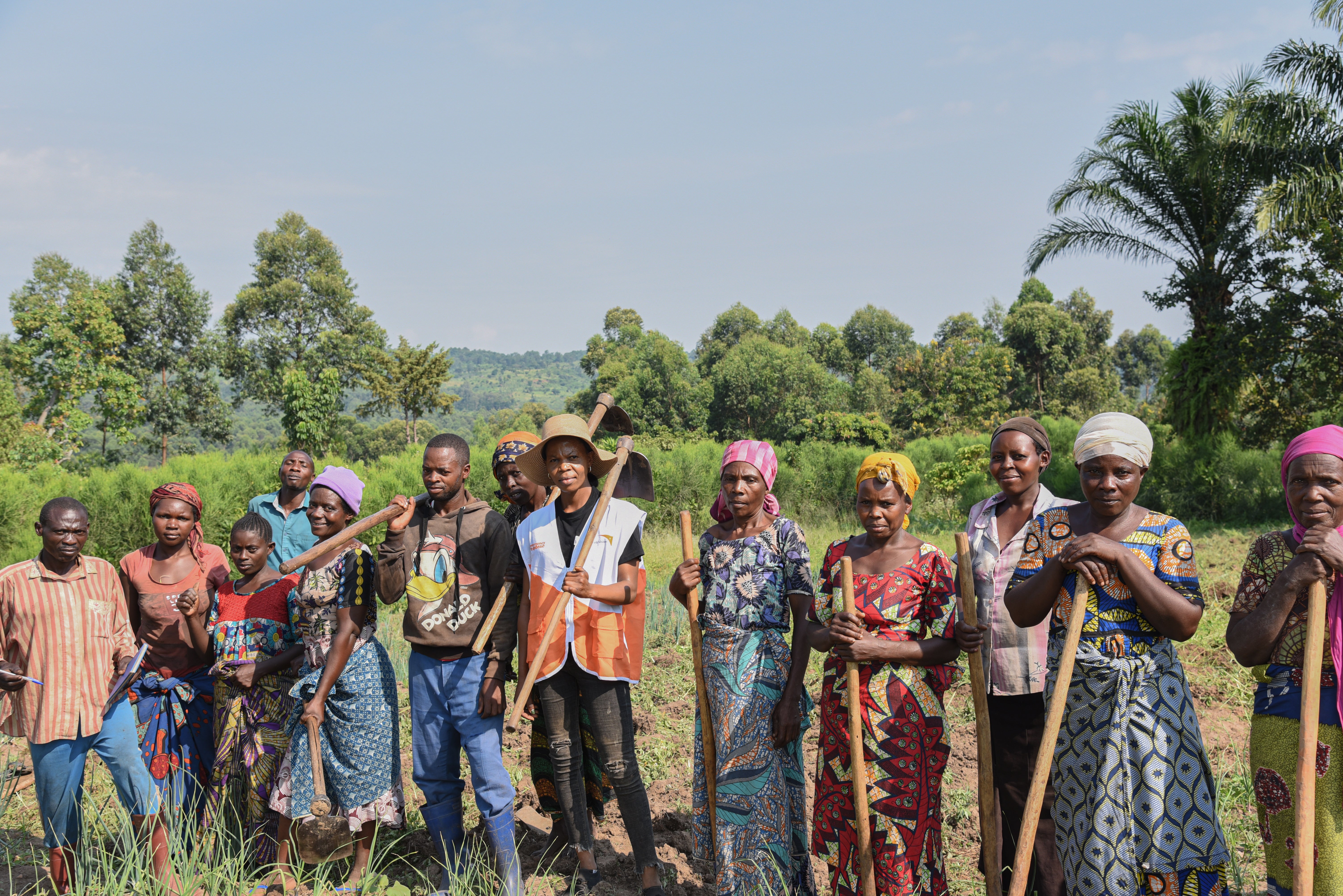 A group of farmers stand together in a field holding shovels and tools. 