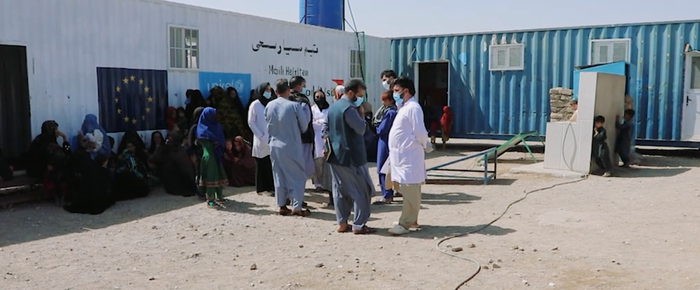A group of men gathered in front of a container truck. Some of them are wearing surgical masks.