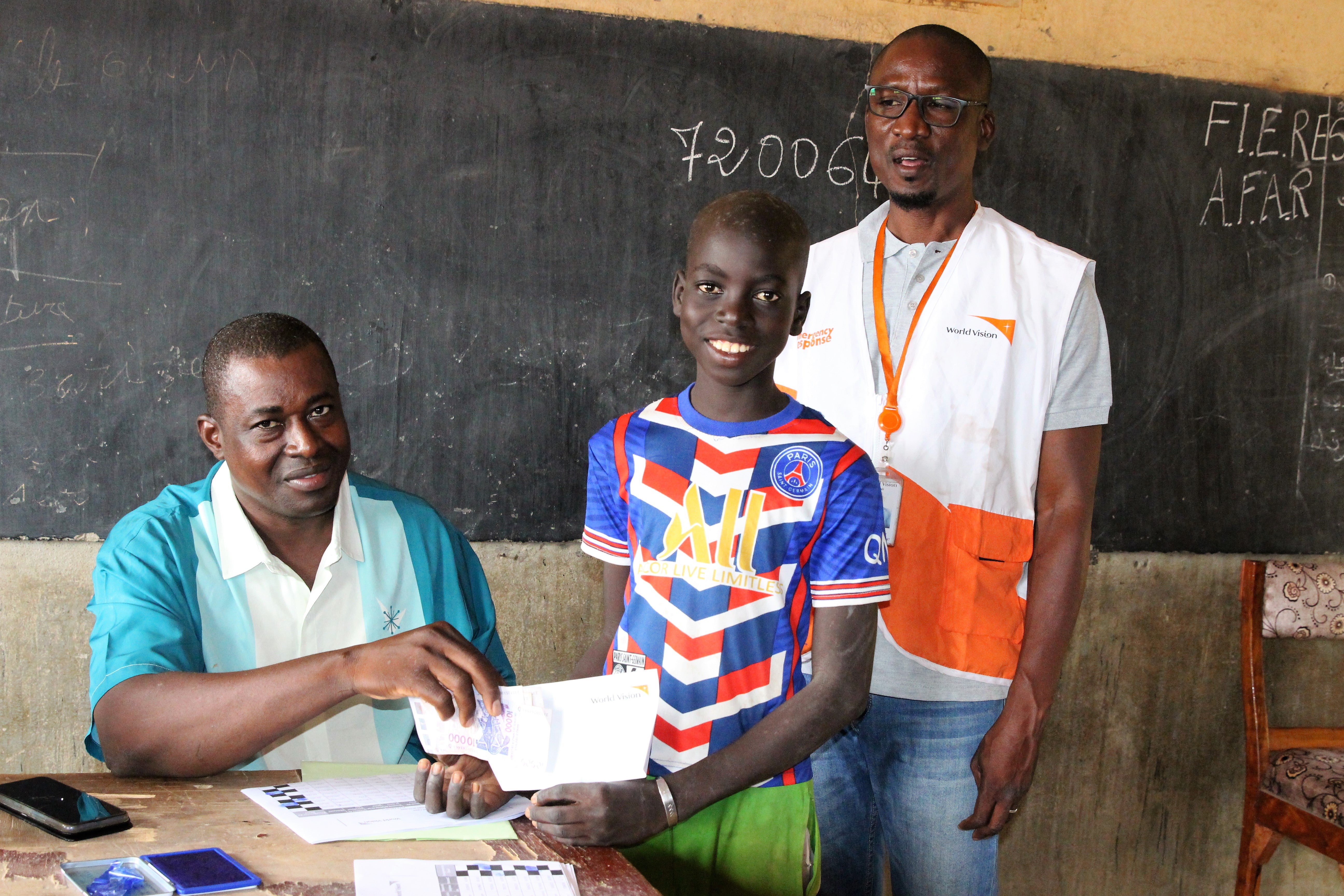 In Mali, a young boy smiles and he holds the cash he received from World Vision staff. 