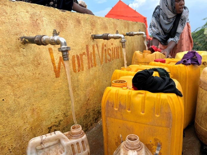 In Somalia, women stand by Water source filling yellow water jugs.  