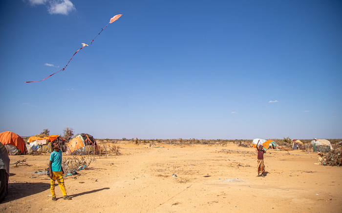 In an Internally Displaced Peron’s camp in Somalia, two children look up at a makeshift kite flying above them.
