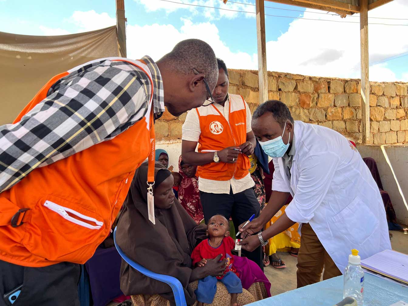A baby receiving a shot in an outdoor medical facility.