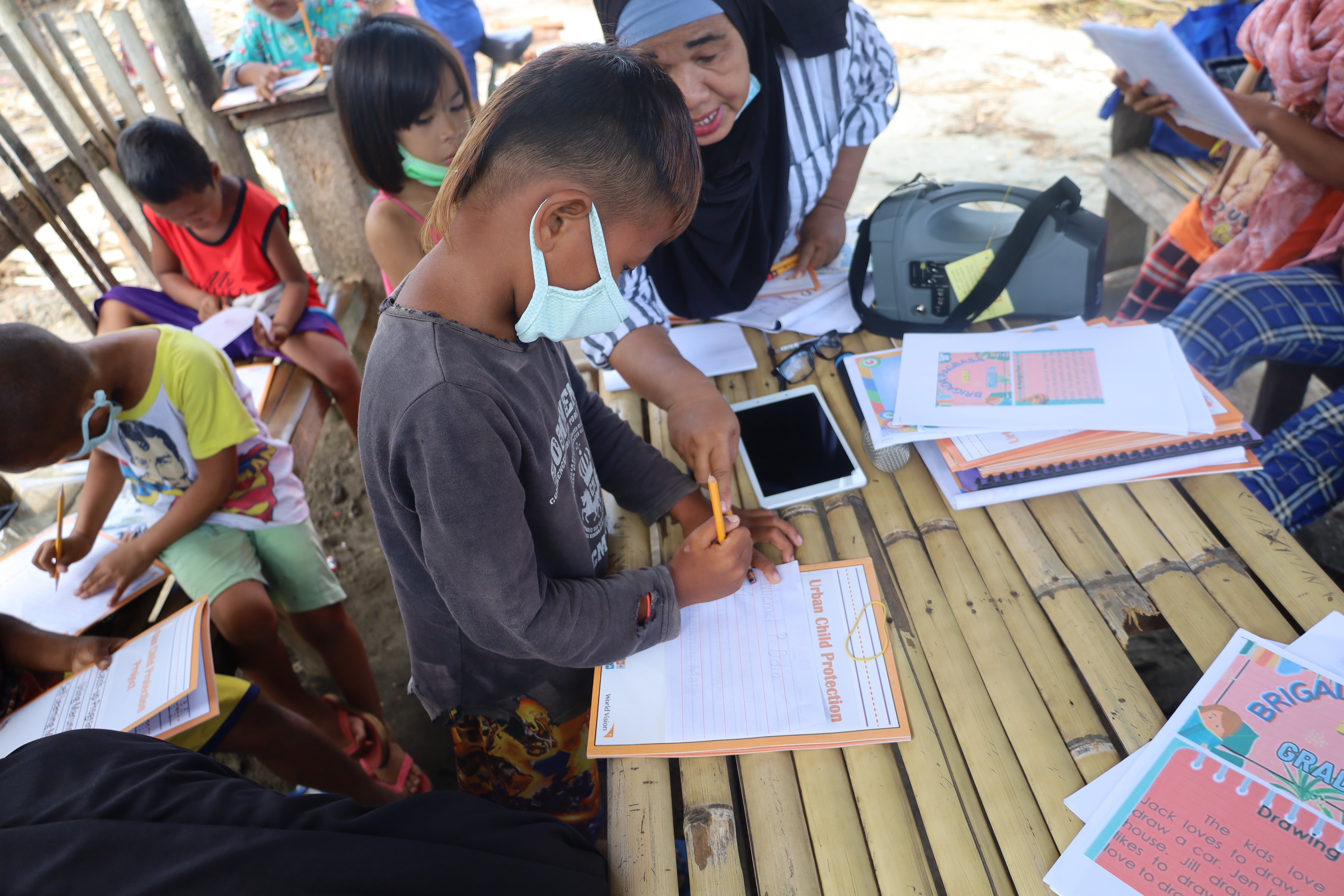 A group of children in an outdoor learning area write in their workbooks.