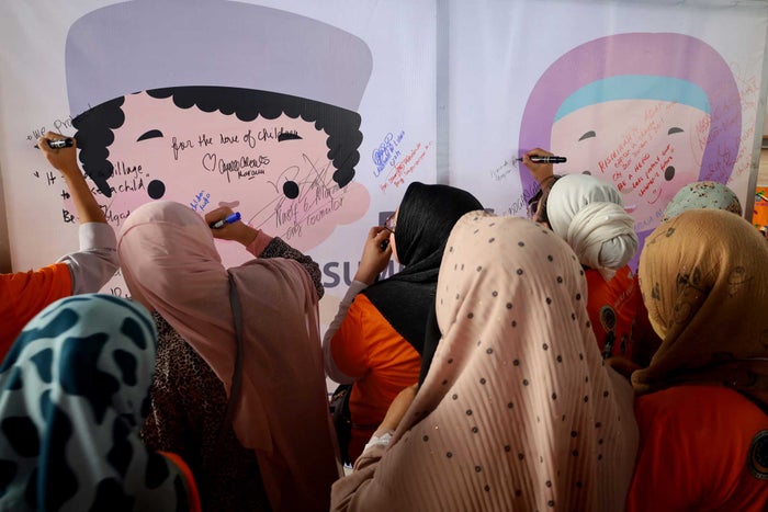 A group of women dressed in head scarves gather around to write notes on a large wall poster. 