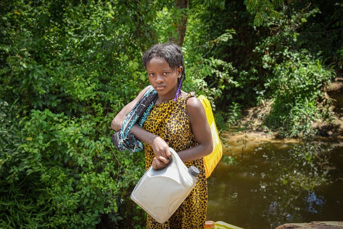 In the Democratic Republic of the Congo, a young girl stands with her water jugs in a jungle