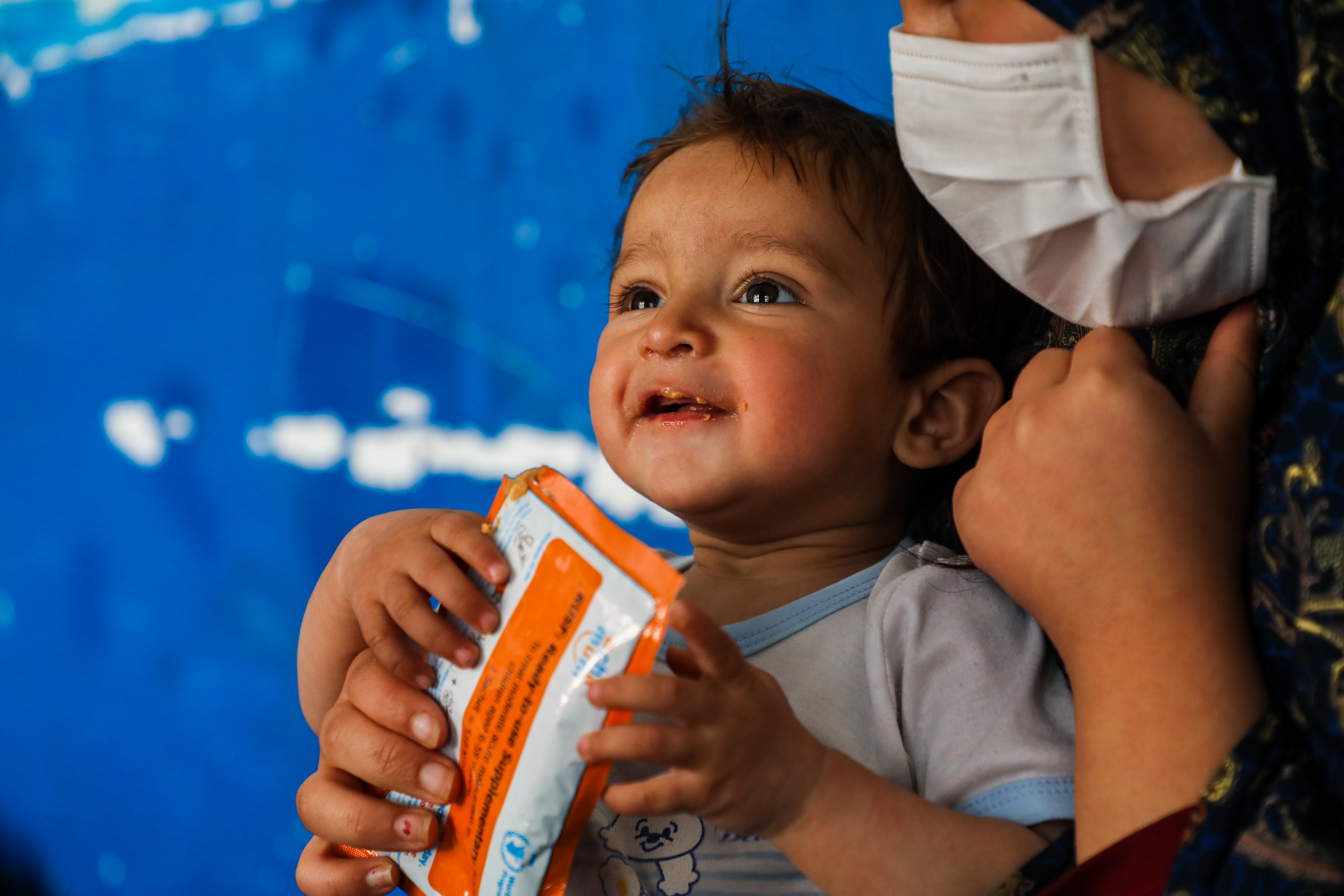 In Afghanistan, a young boy smiles as he sits with his mother, eating from an emergency food supply bag. 