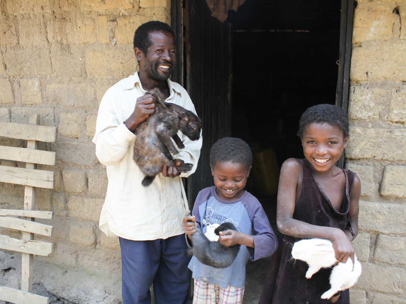 A man and two children, smiling while holding bunnies outside.