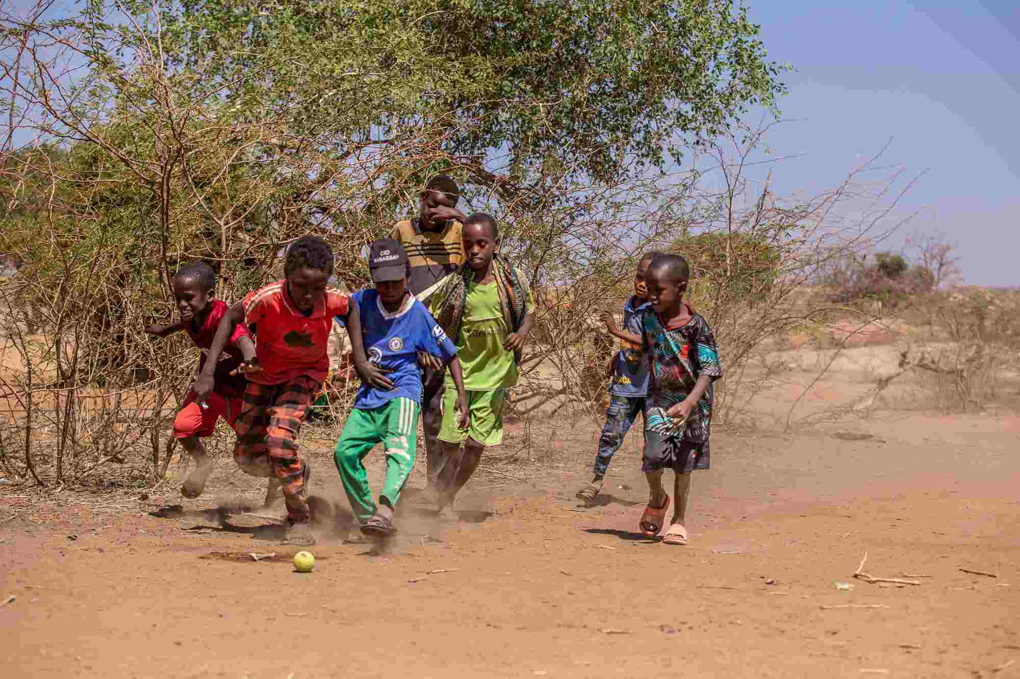 In Somalia, a group of boys play soccer with a small tennis ball on a dirt ground. 