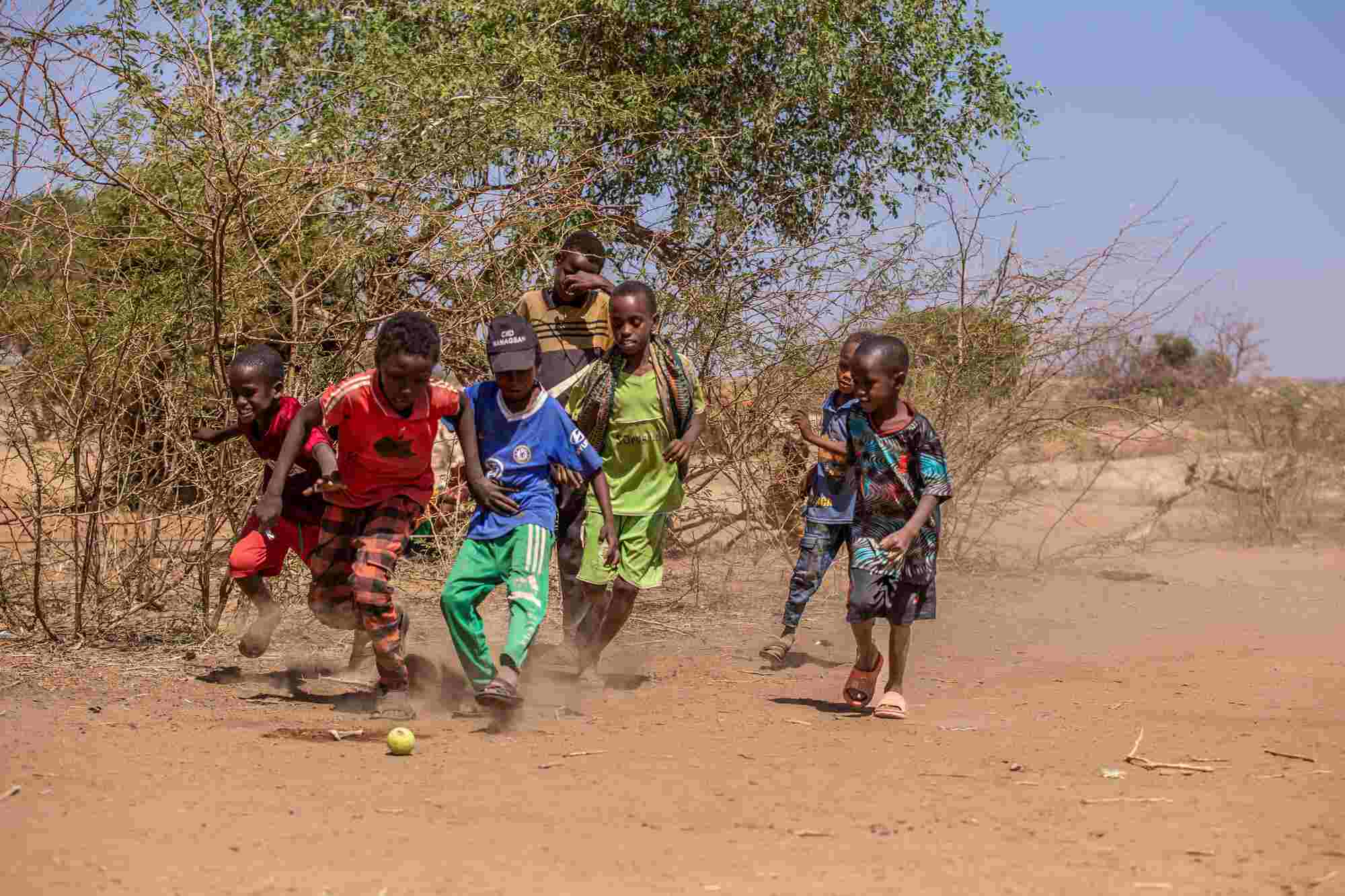 In Somalia, a group of boys play soccer with a small tennis ball on a dirt ground.