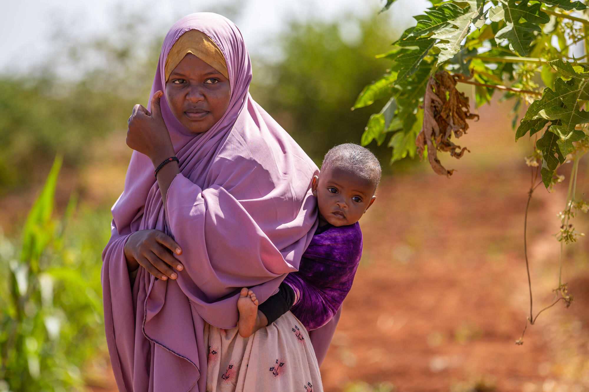 In Doolow, Somalia, a woman carries her child on her back. The World Vision's Kabasa Farm provides long-term solutions to hunger and malnutrition. It is now the source of livelihood for many households who moved to Doolow during the 2011 drought in search of aid and ended up being farmers.