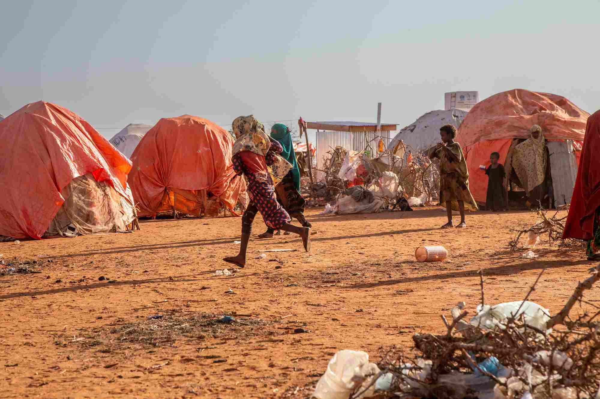 In Somalia, two children run through an Internally Displaced Person’s camp. There are makeshift shelters around them.