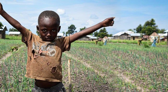 A young boy standing in a crop field, posing for a photo with his arms raised.