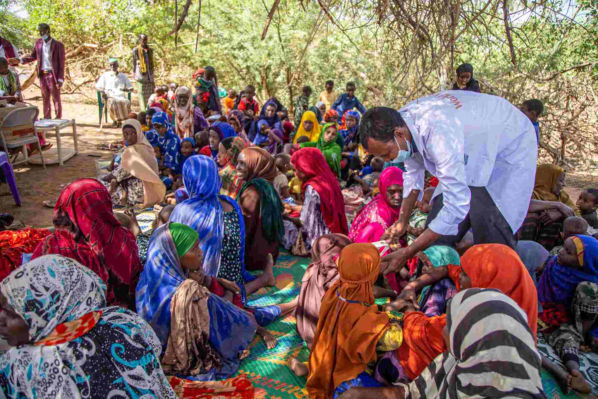 In an Internally Displaced Persons camp in Somalia, a group of people sit on the ground while World Vision staff distribute essential food and supplies. 