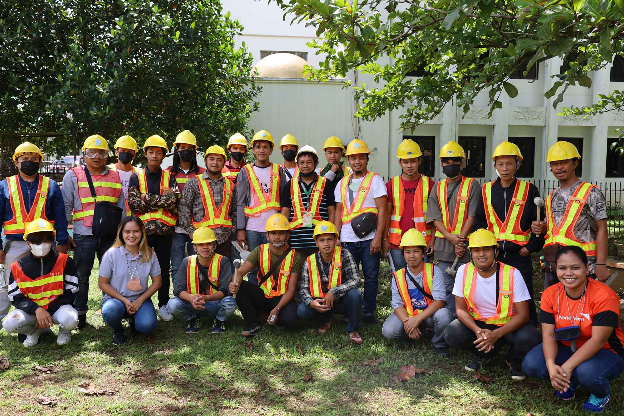 A large group of construction workers wearing hard-hats and safety vests are pictured outside.  