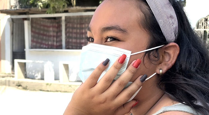 A girl wearing a surgical mask with her hand on her cheek, showing off her painted nails.