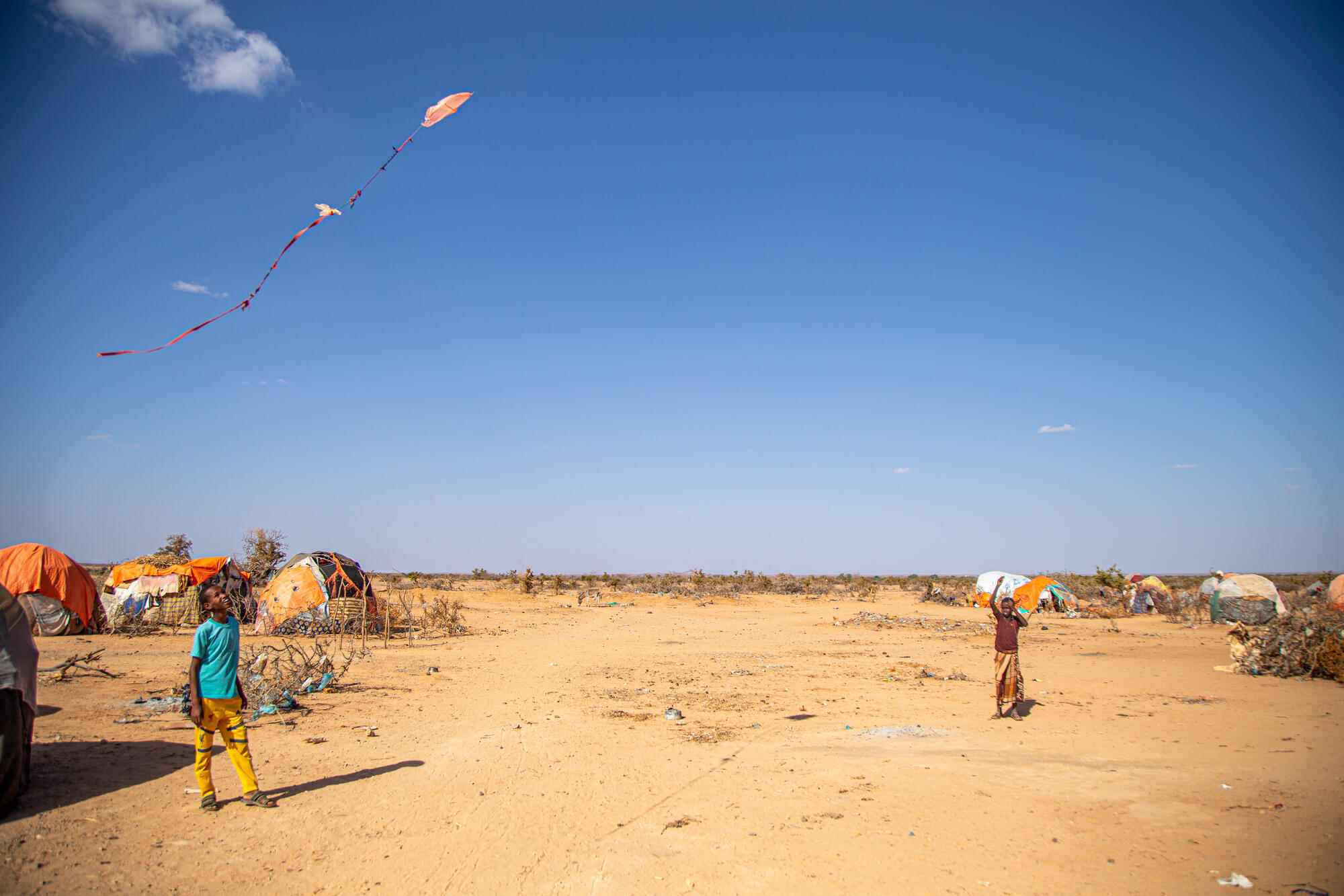 In an Internally Displaced Peron’s camp in Somalia, two children look up at a makeshift kite flying above them.