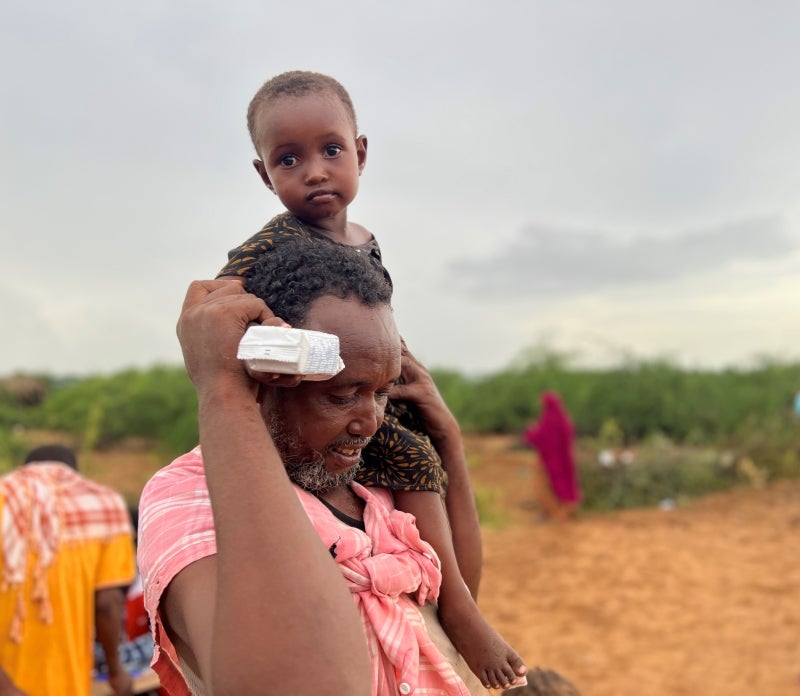 In Somalia, a man carries his daughter on his shoulder. The girl is holding a pack of emergency food. Photo: World Vision, Somalia