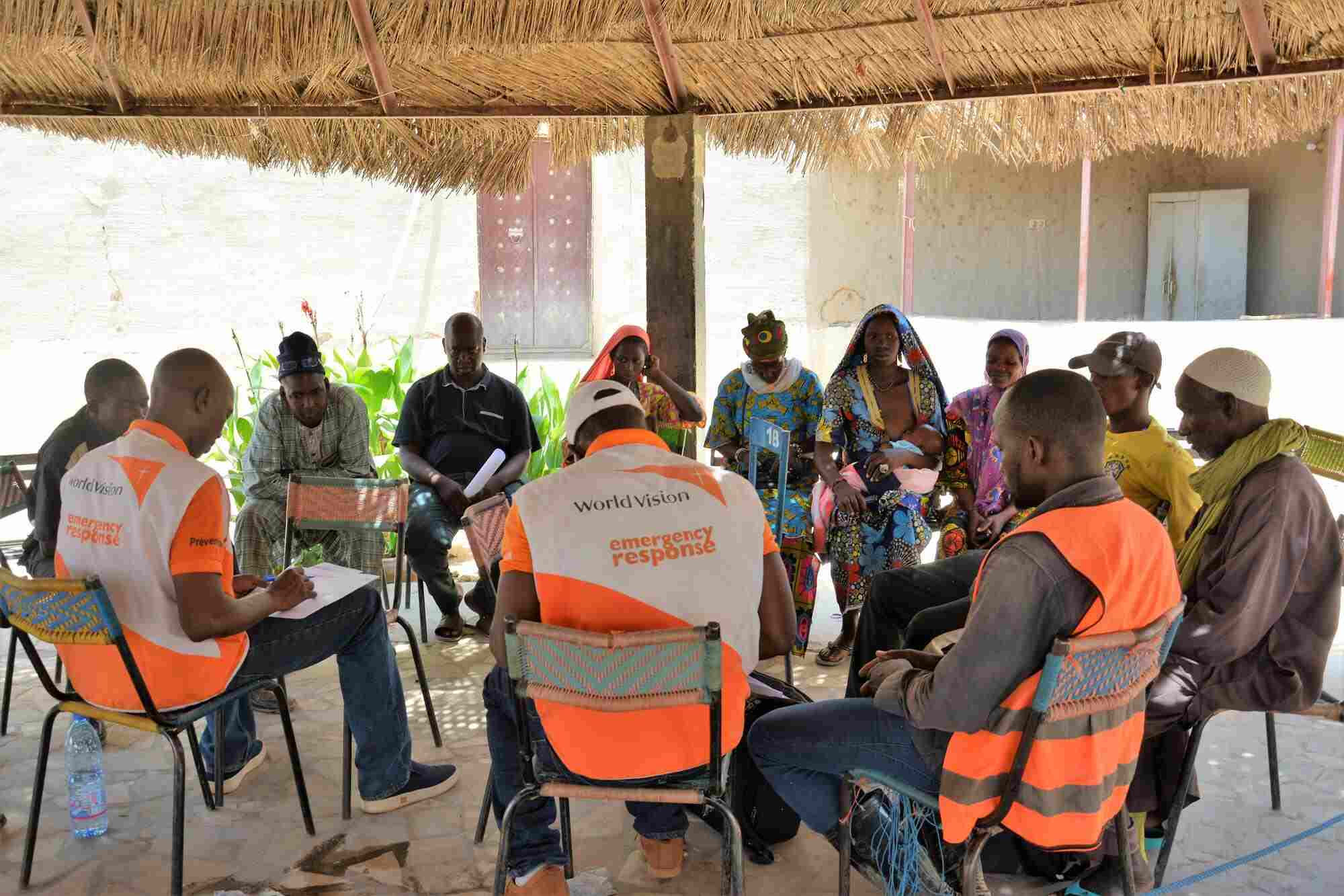 World Vision staff and community members and leaders sit together in a circle. 