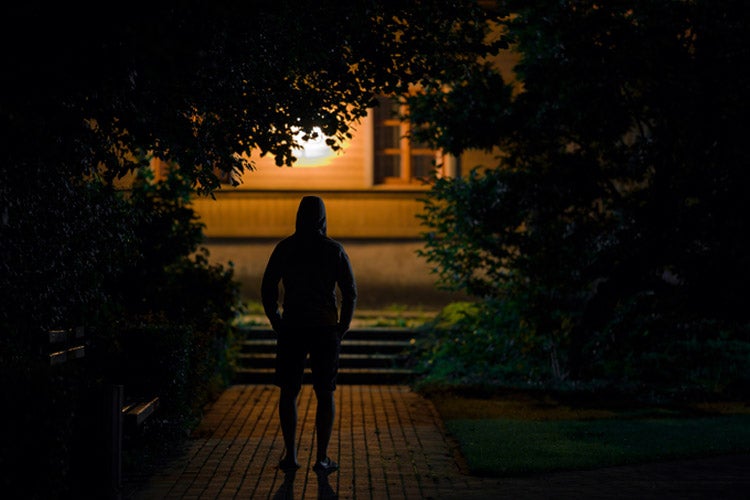 Thief standing on sidewalk in back of home in summer black night. How to protect your Tennessee home from modern burglars.