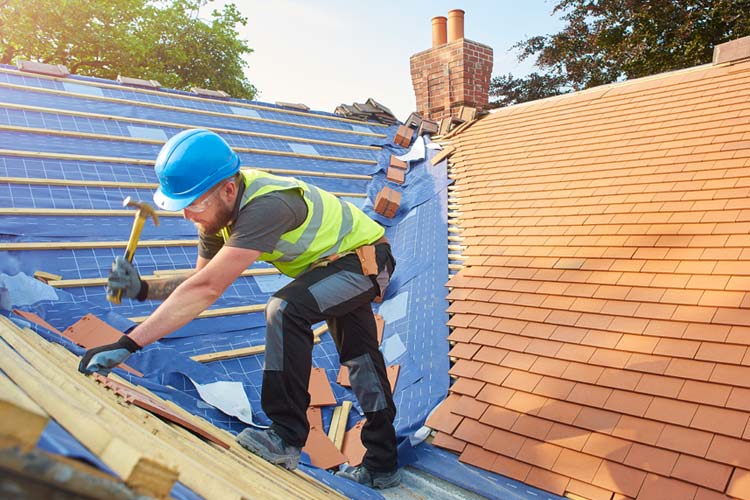 Roofer nails on the roof tiles. Protect Yourself Against Common Roofing Insurance Scams in Florida.