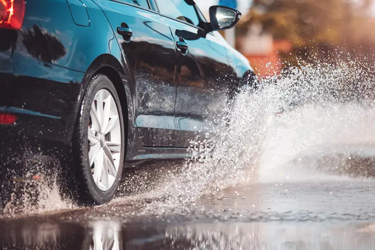 Car driving through the puddle and splashing by water. Will Your Car Insurance Cover Flood Damage? What NJ Drivers Should Know.