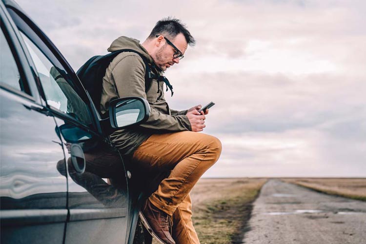 Man leaning on car and using smart phone