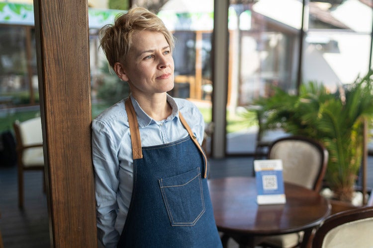 Female small business owner standing in her restaurant alone and thinking. 6 Business Insurance Pitfalls to Avoid in Florida.
