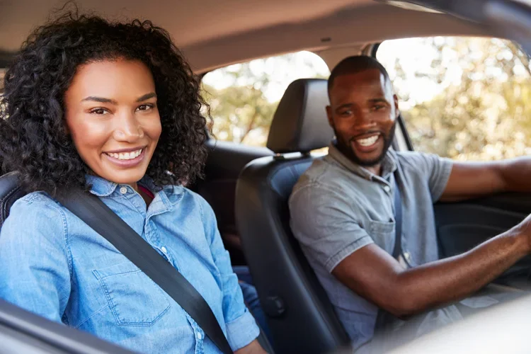 Couple in car on a road trip look ahead smiling. 12 Ways to Reduce Auto Insurance Costs in New Jersey.