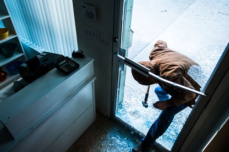 Modern burglar using a sledgehammer to break the glass of a retail store. How to Protect Your Tennessee Business from Modern Burglars. 