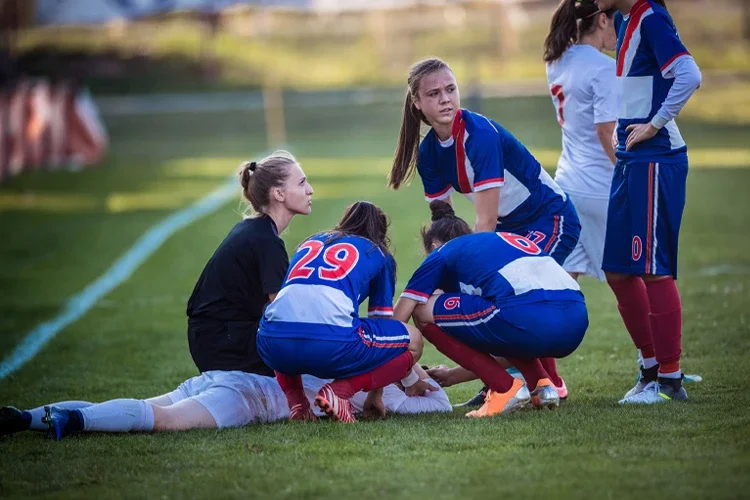 Group of female soccer players and referee gathering around injured player on playing field. If Someone Hurts Another While Playing Sports, Who's Responsible?