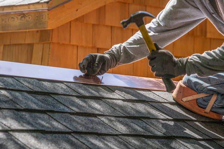 Roofing contractor installing new roof with  nail gun and shingles. How to protect yourself from roofing insurance scams in Tennessee.