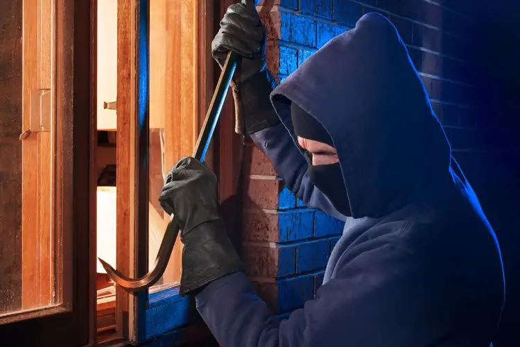 Burglar Using Crowbar To Break Into a House at night. What Property Crimes Does Home Insurance Cover in Mississippi?