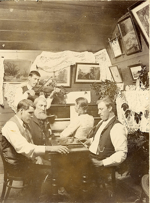 William and Mary Grigor and family in the original Bankfoot House, c1895. Shows Mary playing piano, William and the boys playing a board game - Kenneth on left, William Andrew on right and James playing the violin.