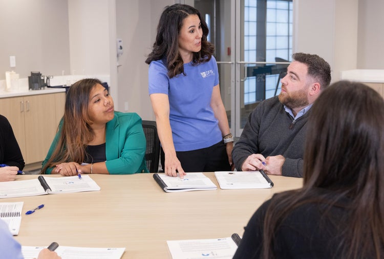 Female trainer explaining something to a participant at the table in the classroom