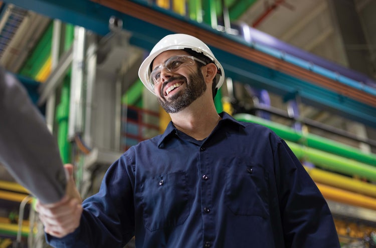 Man, wearing safety helmet and glasses, shaking hands in a plant