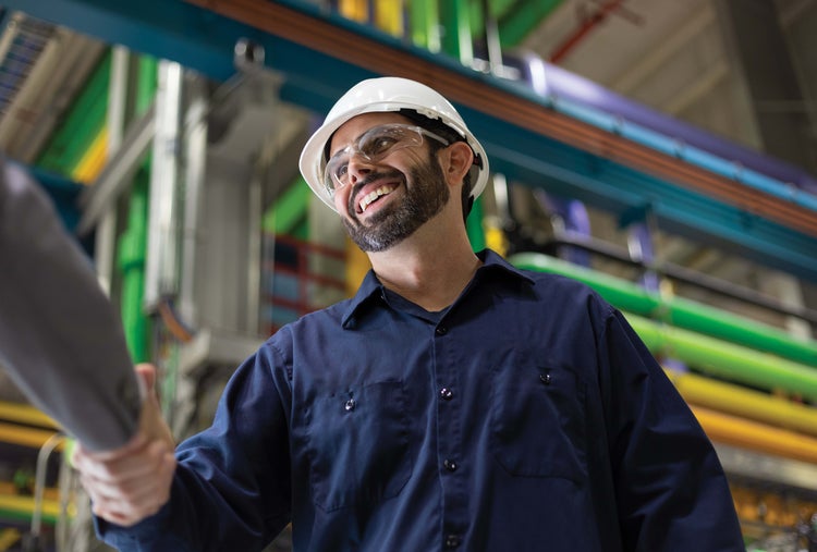 Man, wearing safety helmet and glasses, shaking hands in a plant