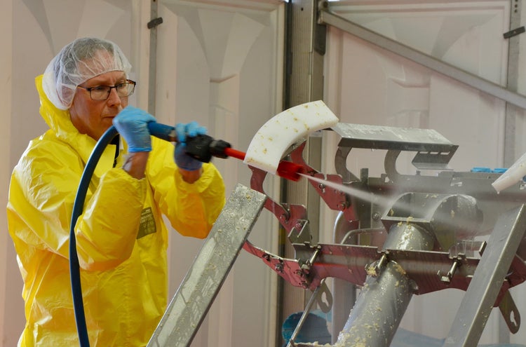 Man in PPE rinsing dirty conveyor