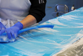 Hands with blue brush, scrubbing conveyor belt during wet cleaning
