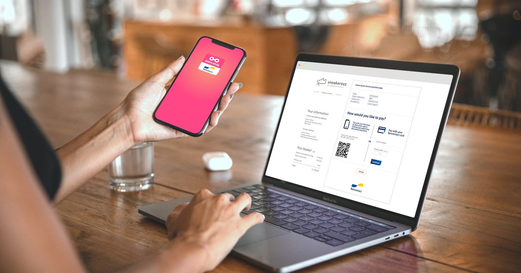A woman with a smartphone in her hand in front of a laptop. The phone has the Payconiq by Bancontact app open and on the laptop there is a Bancontact QR code visible to complete the payment.