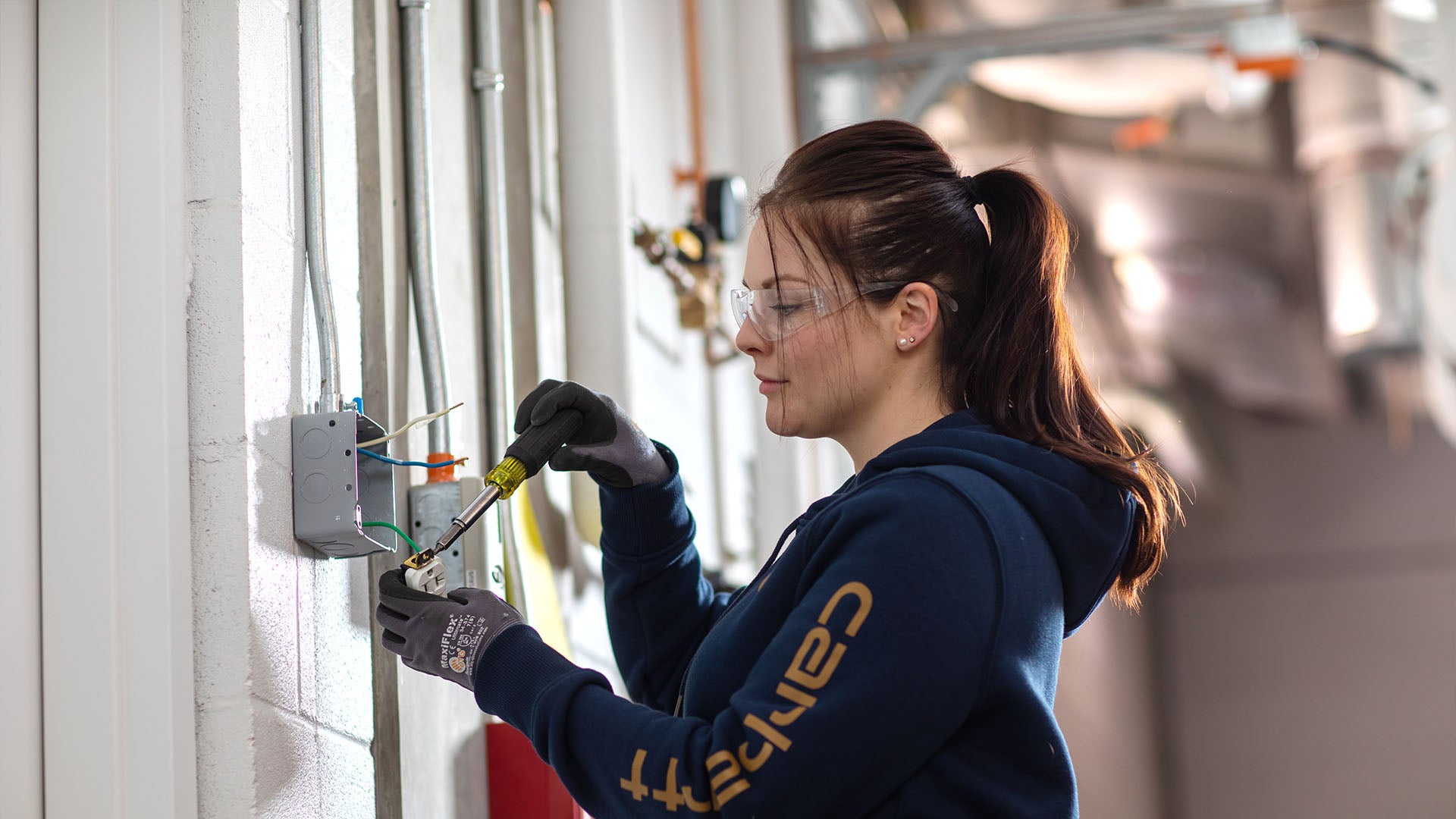 “A female electrician wearing safety glasses uses a screwdriver to work on an electrical outlet. “A female electrician wearing safety glasses uses a screwdriver to work on an electrical outlet.