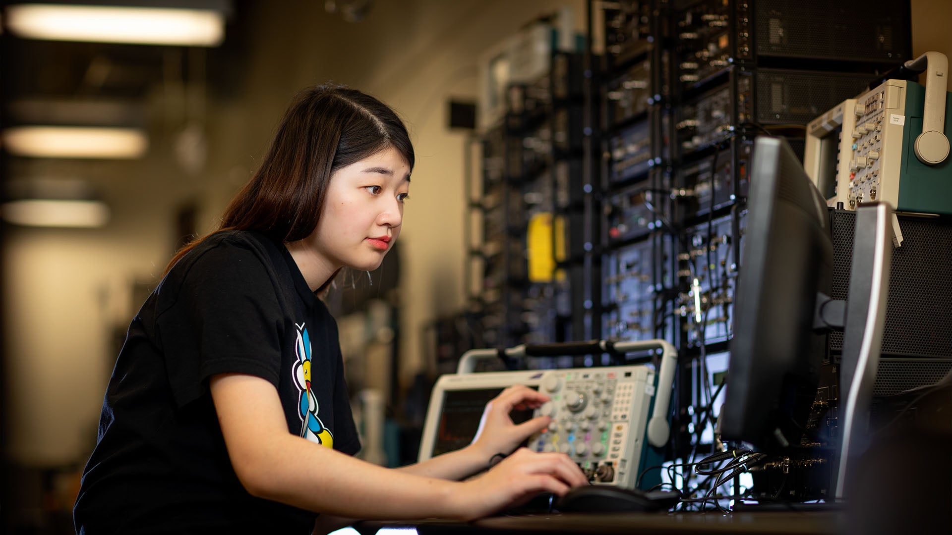 Female student looking at a monitor while working with advanced electronic equipment.