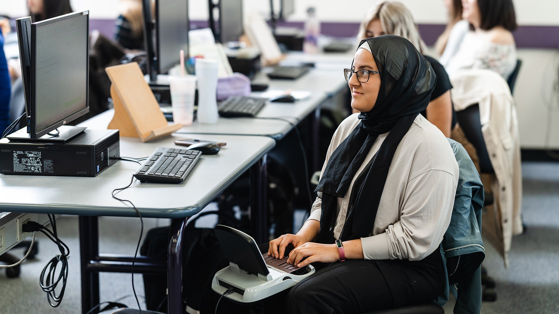 Smiling female student in a classroom typing on a stenography machine.