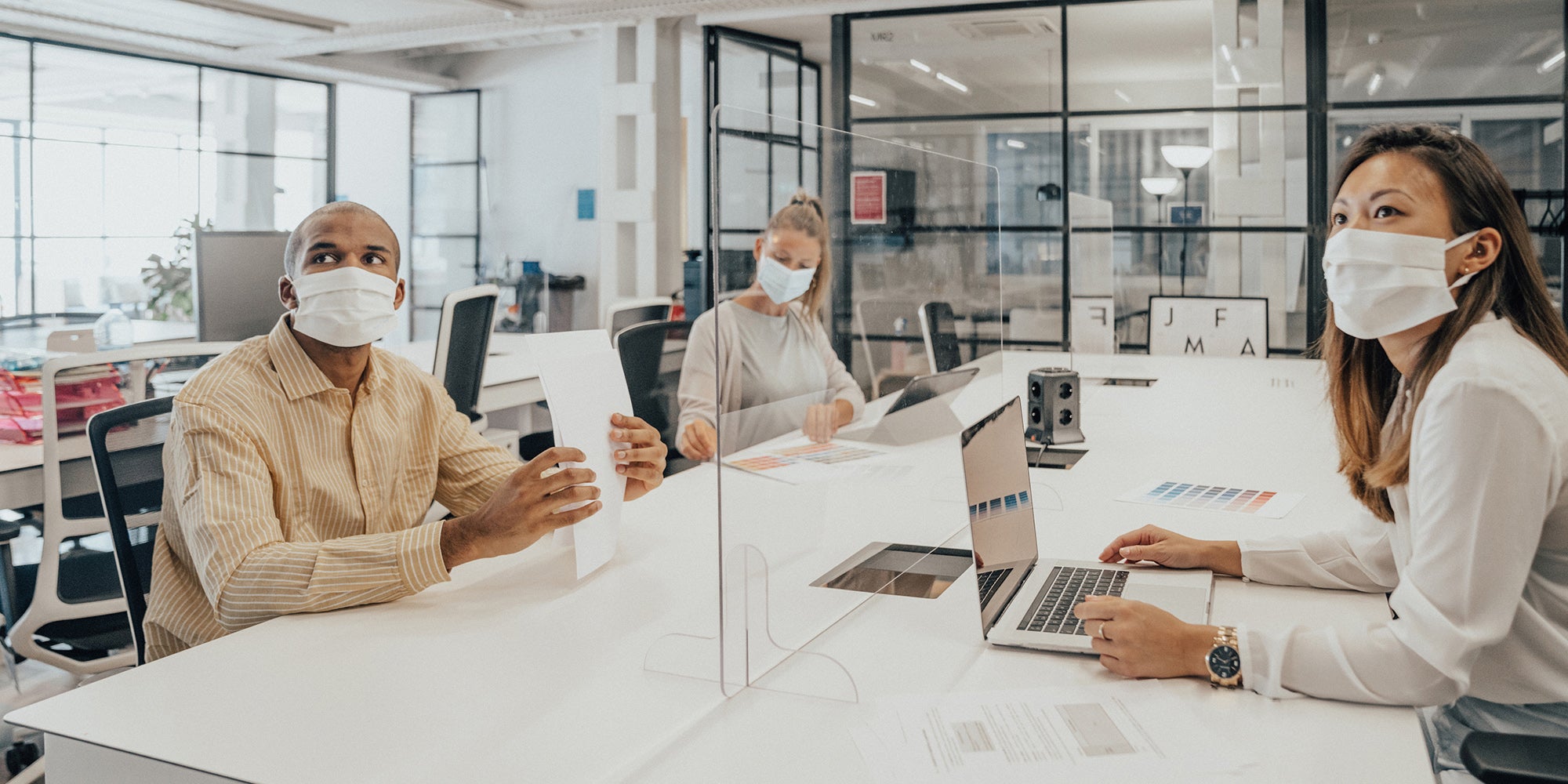 A group of people sitting at a table with a clear screen A group of people sitting at a table with a clear screen
