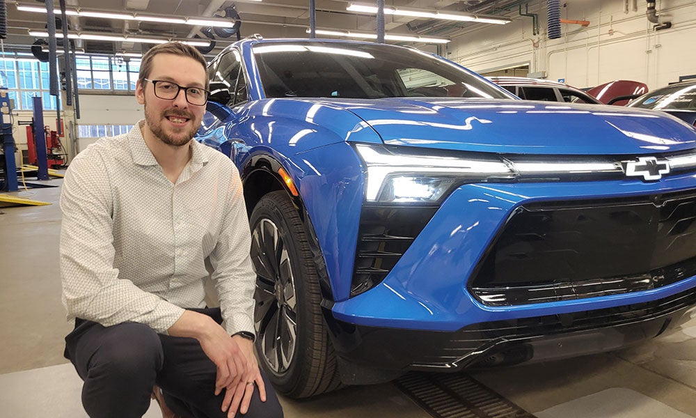 A man sitting next to a blue car
