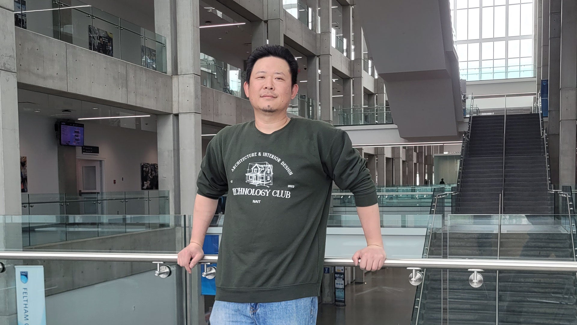Person standing indoors at a modern building balcony, holding a railing with a staircase and glass architecture in the background. Person standing indoors at a modern building balcony, holding a railing with a staircase and glass architecture in the background.