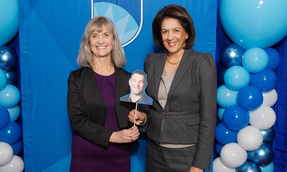 Two women holding a cardboard cutout of a man's face