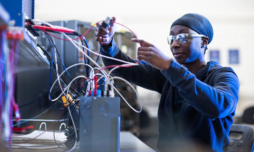 A woman wearing safety goggles and holding electrical wires