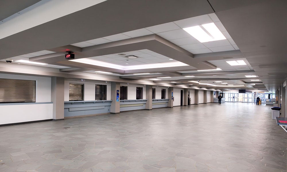 Large open lobby area with service counters along one wall, a patterned tile floor, and a modern ceiling design extending toward glass entrance doors.